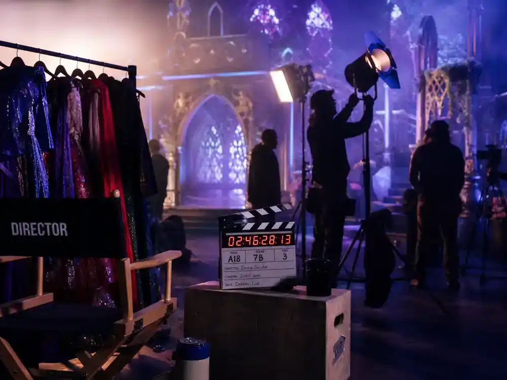 Disney Plus movies and shows July 2026 Descendants Wicked Wonderland — musical film set with costume rack and director chair silhouettes from behind