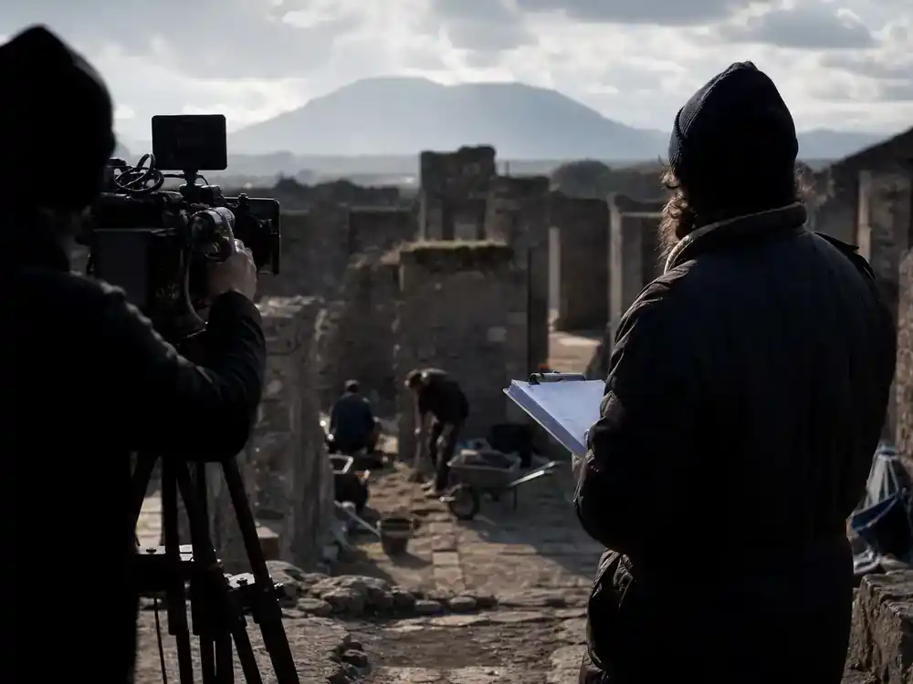 Disney Plus movies and shows July 2026 Pompeii documentary — film crew silhouettes on ancient ruins location shoot, photojournalistic documentary production