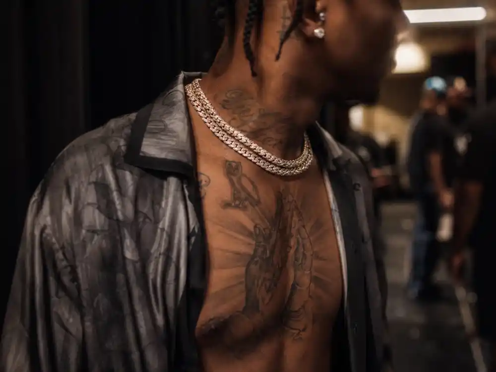 Drake tattoos and their meanings — chest praying hands and owl tattoos visible over-shoulder on hip-hop musician backstage