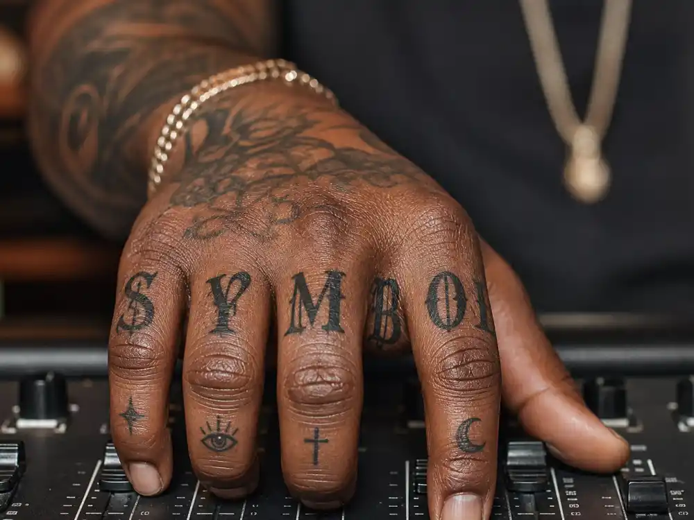 Drake tattoos and their meanings — tattooed fingers and knuckles with SYMBOL lettering on artist hands at studio console