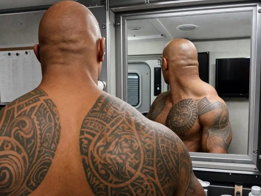 Dwayne Johnson tattoos and their meanings — warrior face Polynesian chest tattoo over heart area over-shoulder view