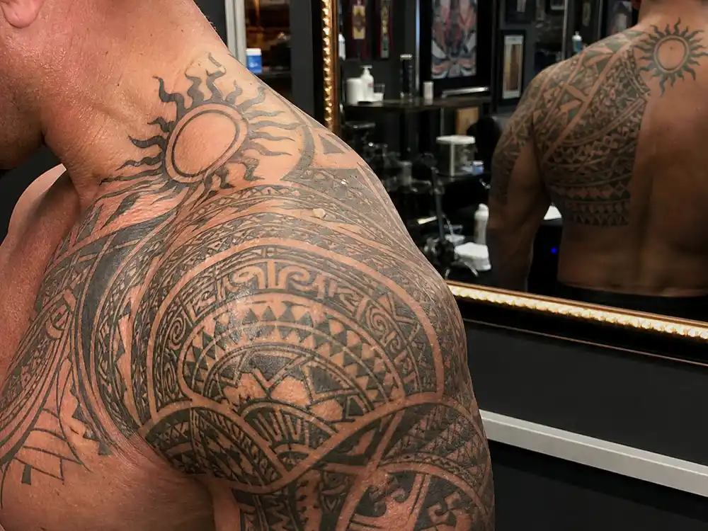 Dwayne Johnson tattoos and their meanings — close-up of Polynesian tribal tattoo on left shoulder chest and arm with sun symbol