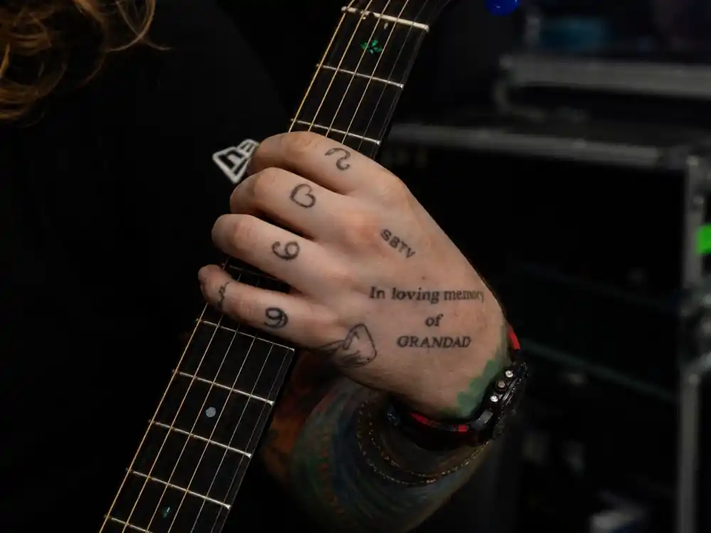 Ed Sheeran tattoos and their meanings hand ink — Michael and Jamal memorial tattoos on guitar-playing left hand close-up