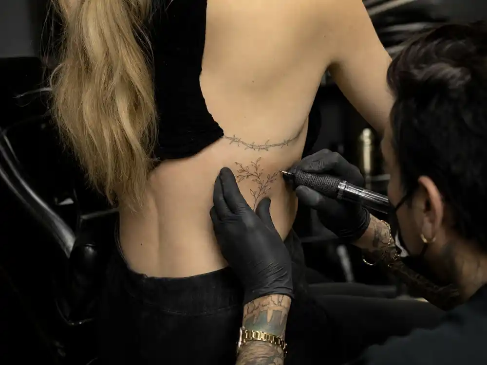 Ellie Goulding tattoos and their meanings Dr Woo — Shamrock Social Club LA studio session with artist gloved hands applying fine-line ribcage ink