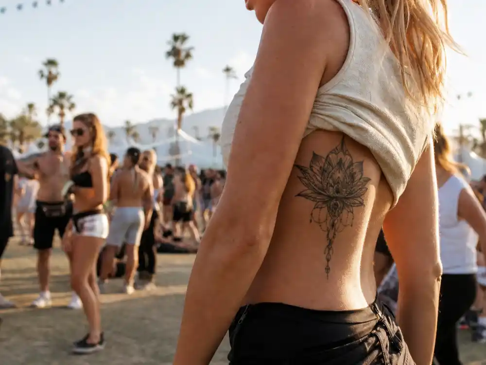Ellie Goulding tattoos and their meanings lotus — fine-line black lotus flower tattoo on right ribcage at Coachella festival golden hour