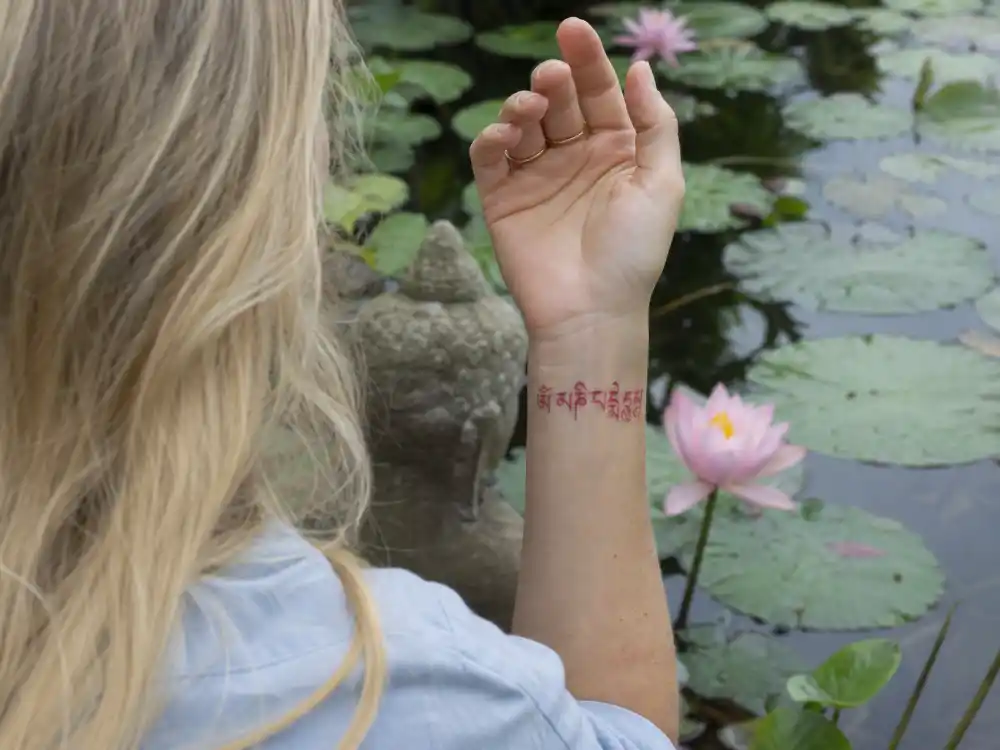 Ellie Goulding tattoos and their meanings Tibetan — red Om mani padme hum mantra tattoo on left wrist over-shoulder at lotus garden