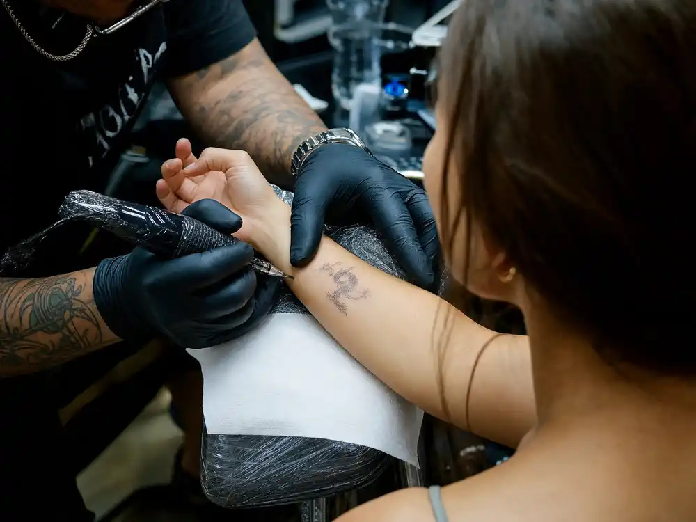 Emilia Clarke tattoos and their meanings Dr Woo — celebrity tattoo artist applying fine-line dragon ink during professional wrist session