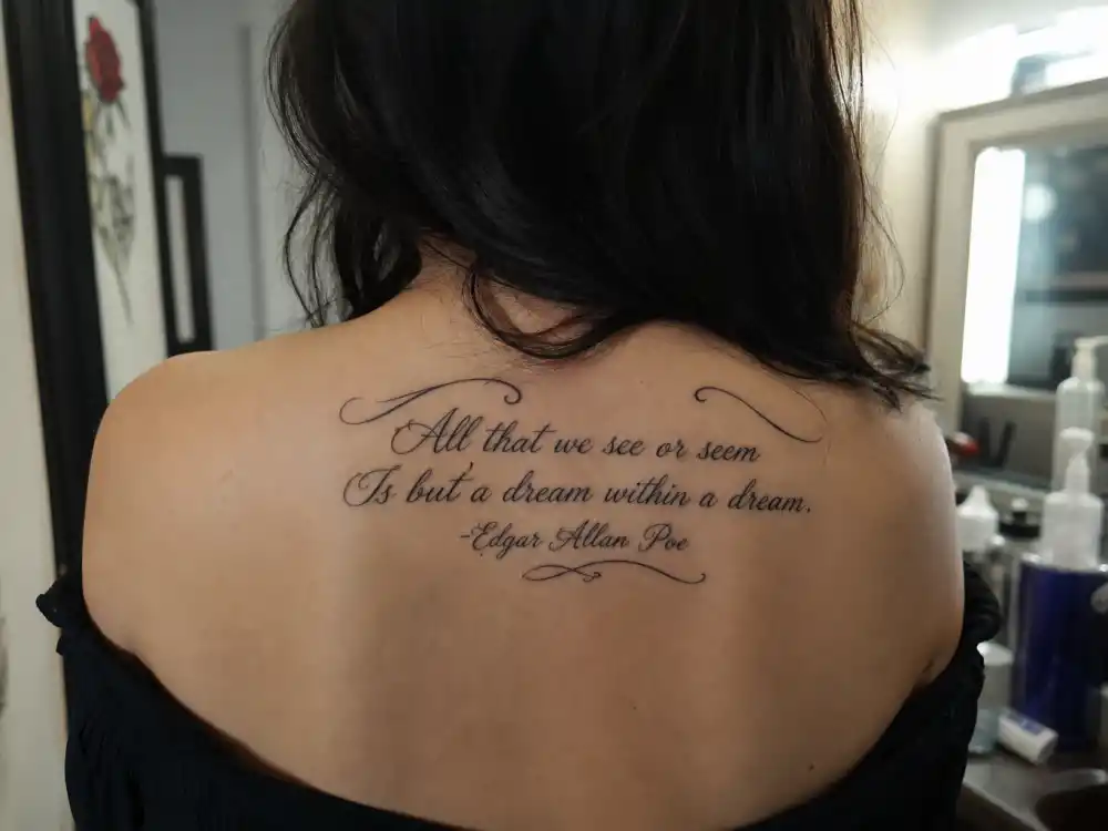 Evan Rachel Wood tattoos and their meanings Poe back — upper back script tattoo reading dream within a dream quote in calligraphic ink