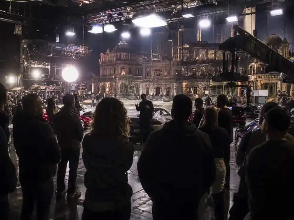 Fast and Furious cast net worth 2026 ranked Dwayne Johnson — actor silhouettes from behind reviewing scripts on director chairs at action film set