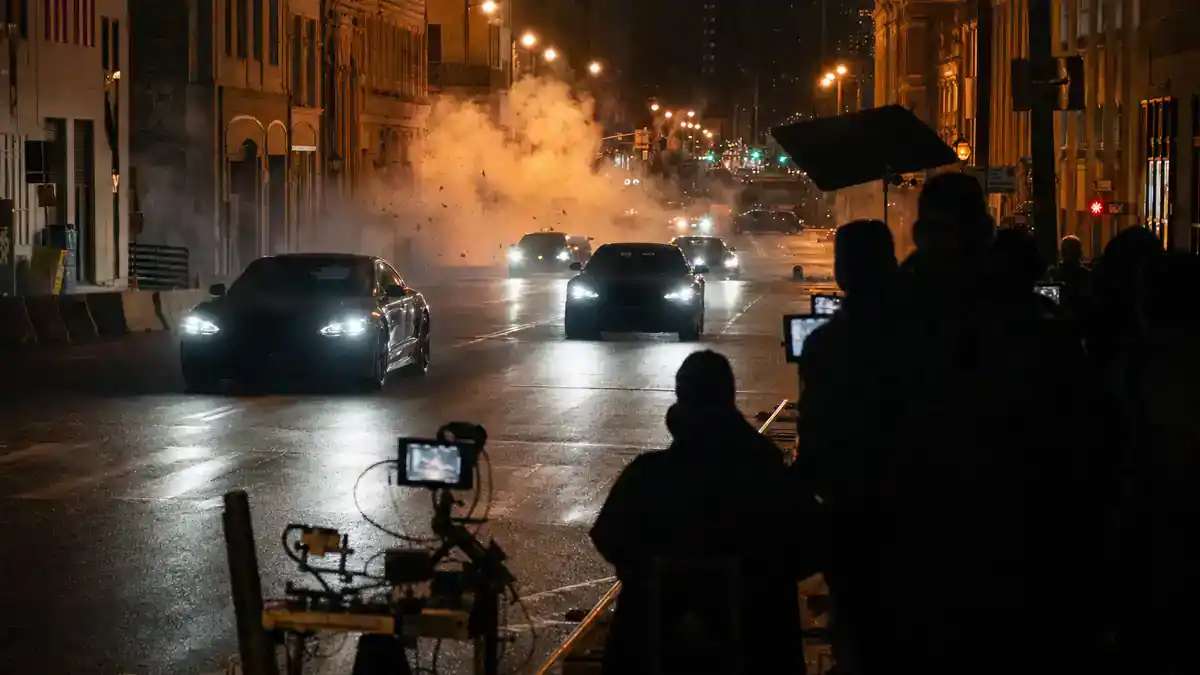 Fast and Furious cast net worth 2026 ranked — night car stunt filming with crew silhouettes and generic sports cars on closed street, editorial production reference