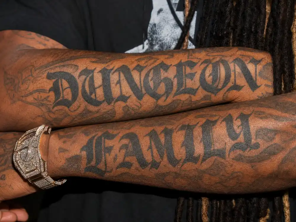 Future tattoos and their meanings — close-up of DUNGEON and FAMILY Olde English forearm tattoos matching Rico Wade Dungeon Family markings