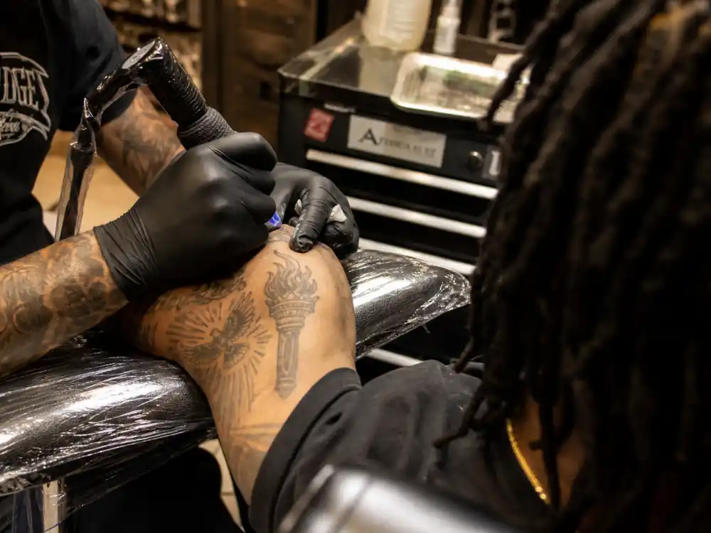 Future tattoos and their meanings — tattoo artist session working on forearm torch and bird ink on dreadlocked client
