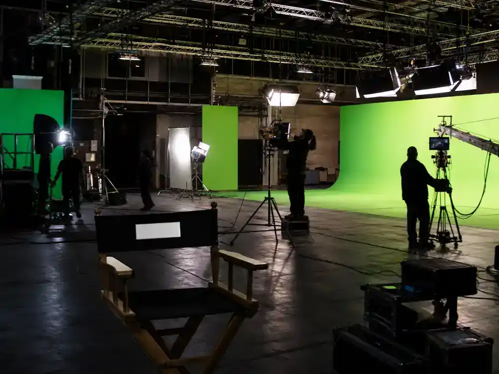 Game of Thrones filming locations in Ireland guide Belfast studios — indoor TV drama soundstage with lighting rigs director chair and crew silhouettes at Paint Hall style facility