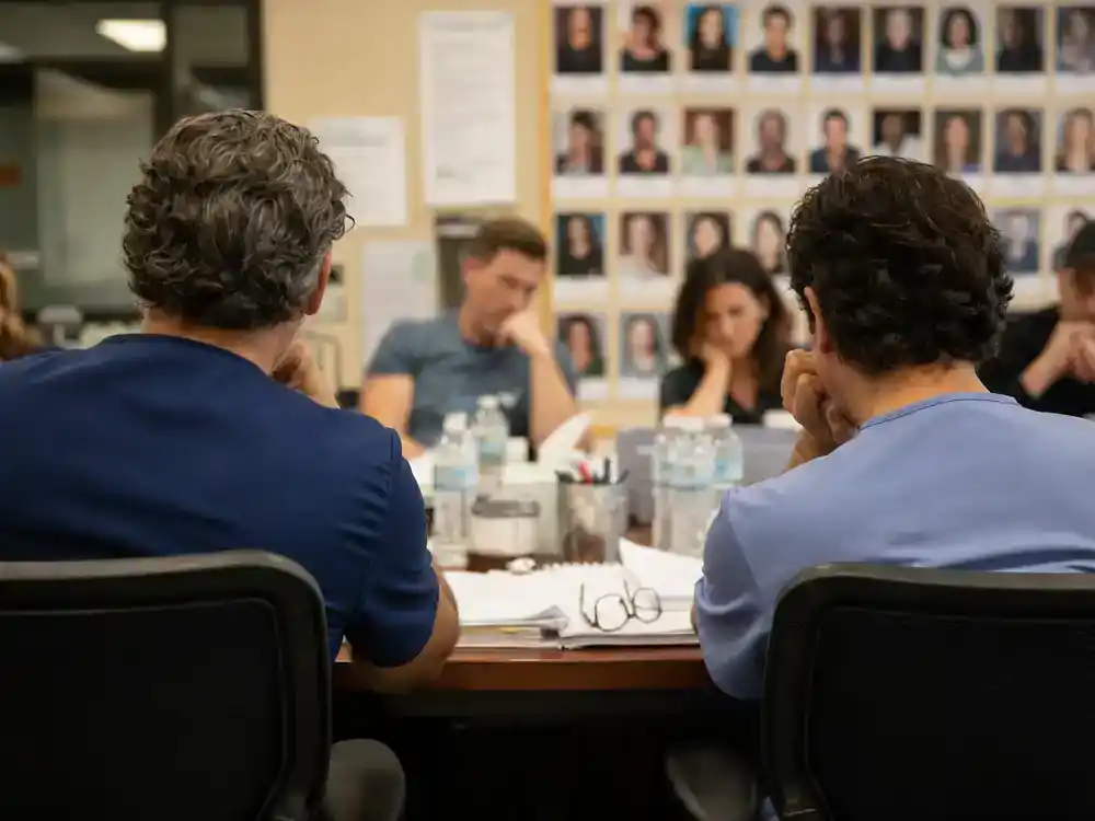 Grey's Anatomy season 22 cast and returning stars Bailey Webber veterans — two actor silhouettes from behind at medical drama table read with scripts on conference table