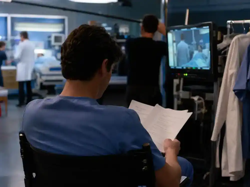 Grey's Anatomy season 22 cast and returning stars Meredith Grey — actor silhouette from behind on director chair reviewing script at hospital drama soundstage