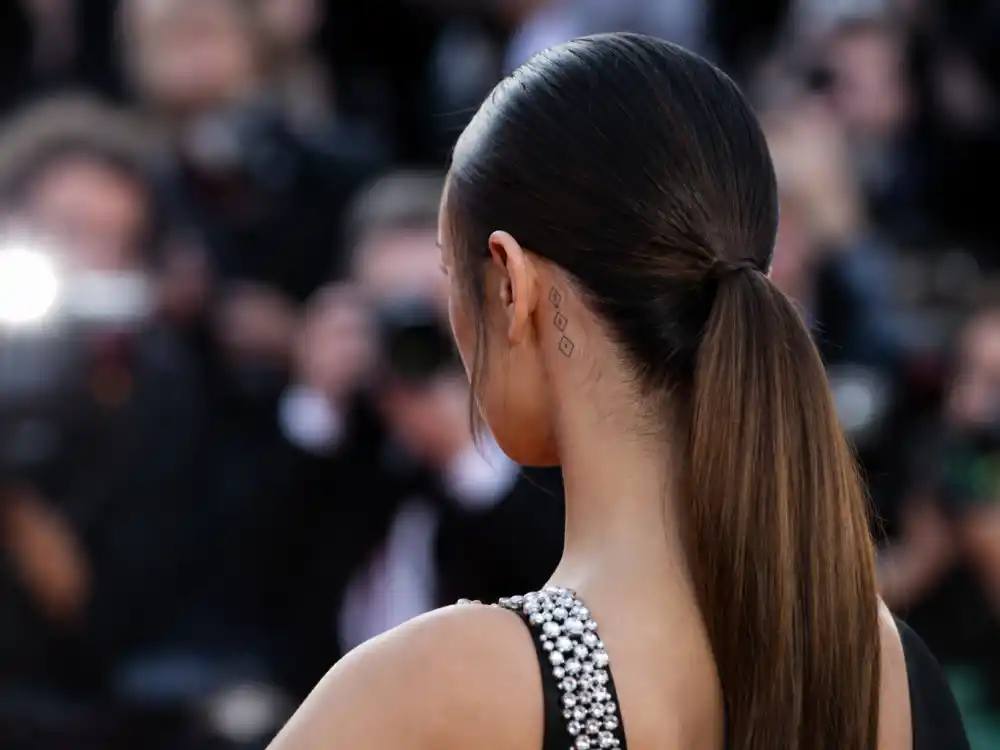 Hailey Bieber tattoos and their meanings diamond ear — tiny geometric diamond shape tattoos behind ear along hairline over-shoulder premiere angle