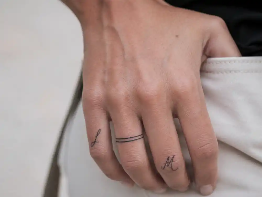 Hailey Bieber tattoos and their meanings finger ink — fine-line wedding band tattoo and letter script on ring finger and hand close-up