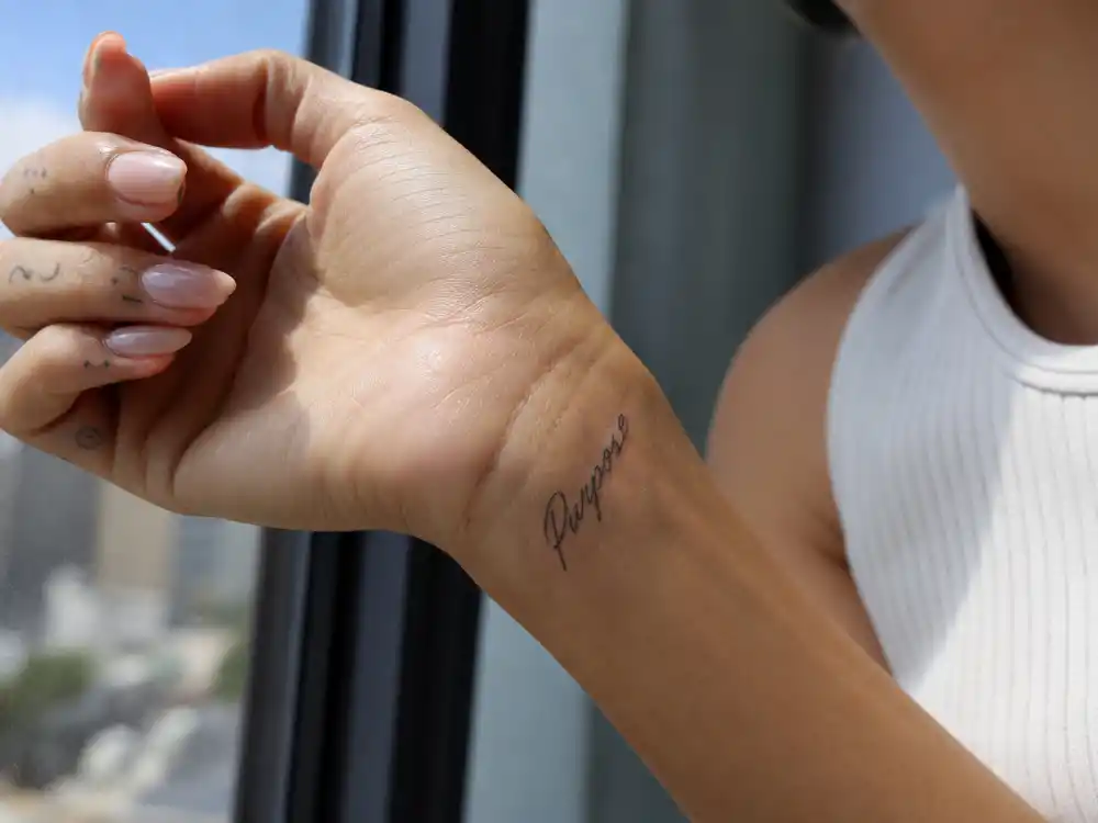 Hailey Bieber tattoos and their meanings Purpose wrist — fine-line Purpose script tattoo on inner wrist with delicate finger ink visible