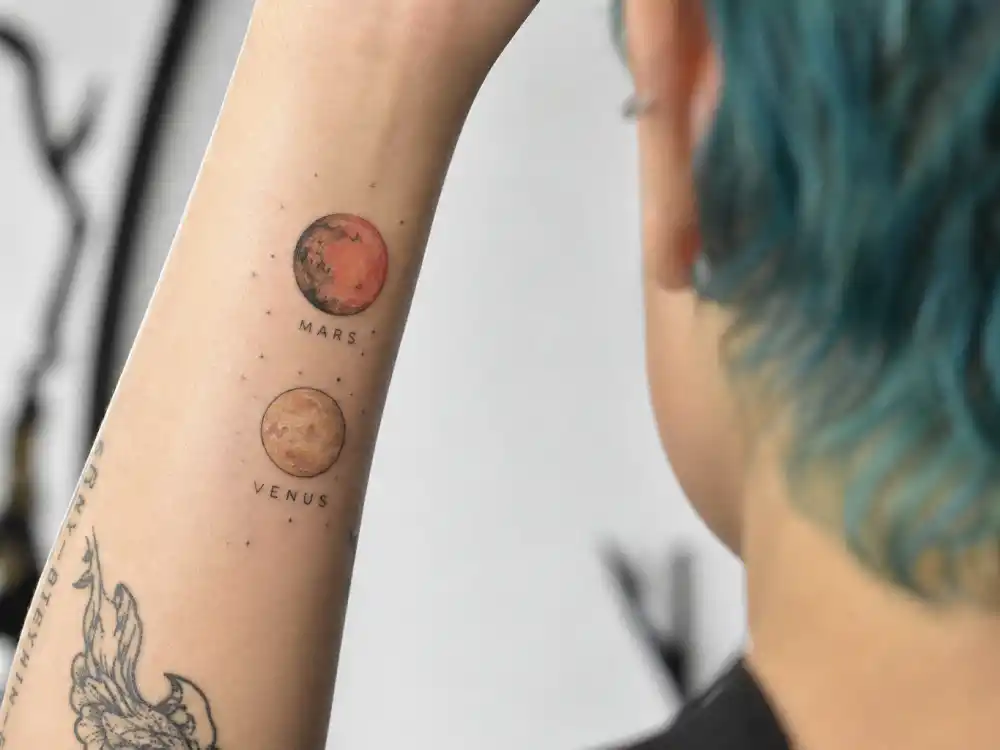 Halsey tattoos and their meanings — fine-line Mars and Venus planet tattoos on forearm photographed from behind