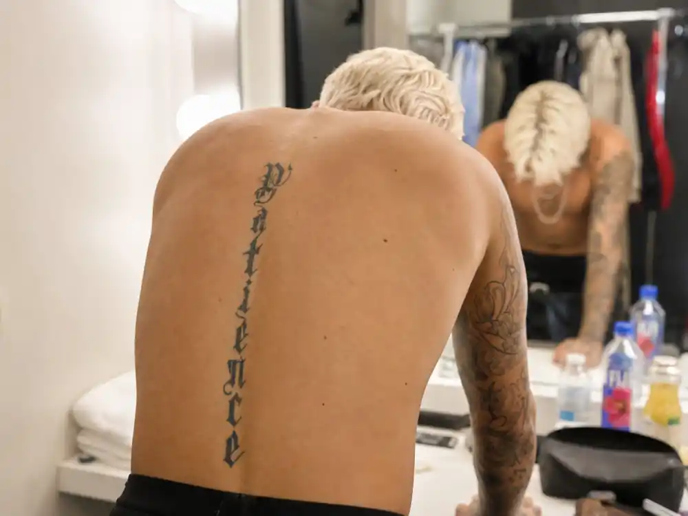Halsey tattoos and their meanings — bold NIGHTMARE spine lettering tattoo visible along upper back in backstage mirror