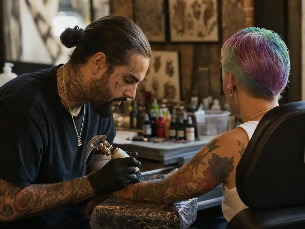 Halsey tattoos and their meanings — tattoo artist inking colorful forearm sleeve during professional studio session