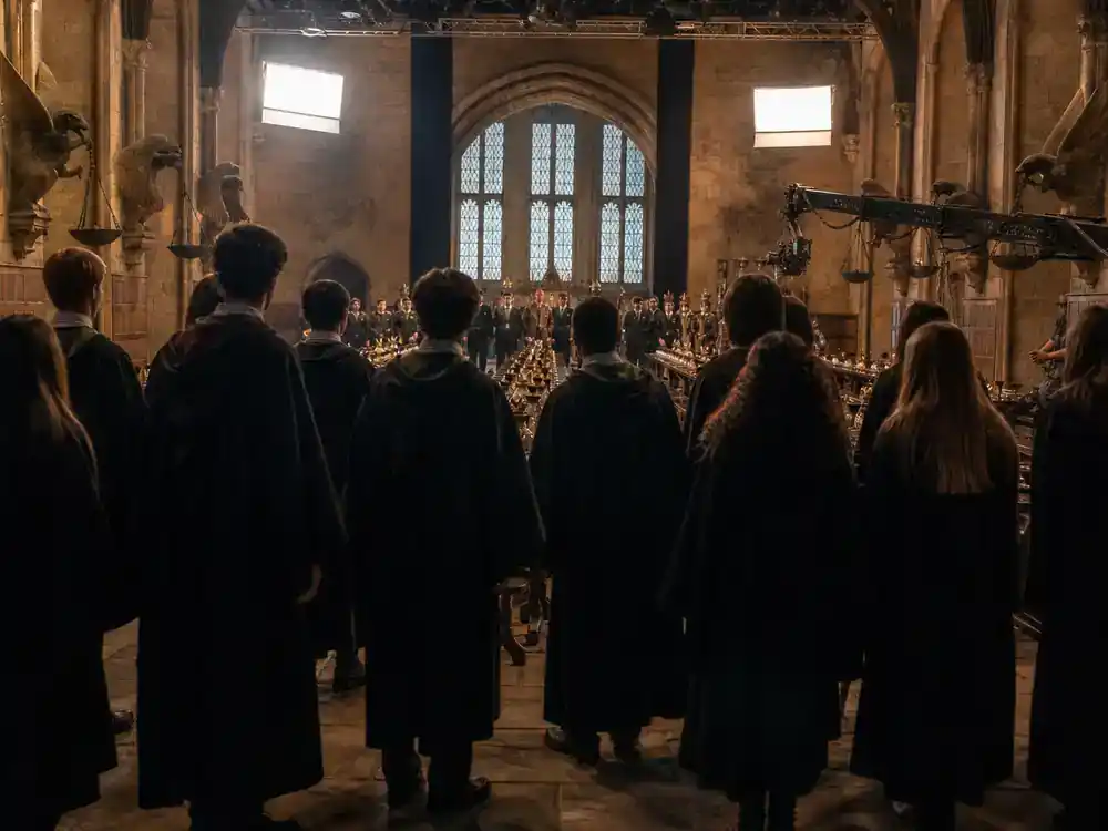 Harry Potter cast net worth 2026 ranked ensemble — cast silhouettes from behind rehearsing on grand hall film set with long tables and lighting rigs
