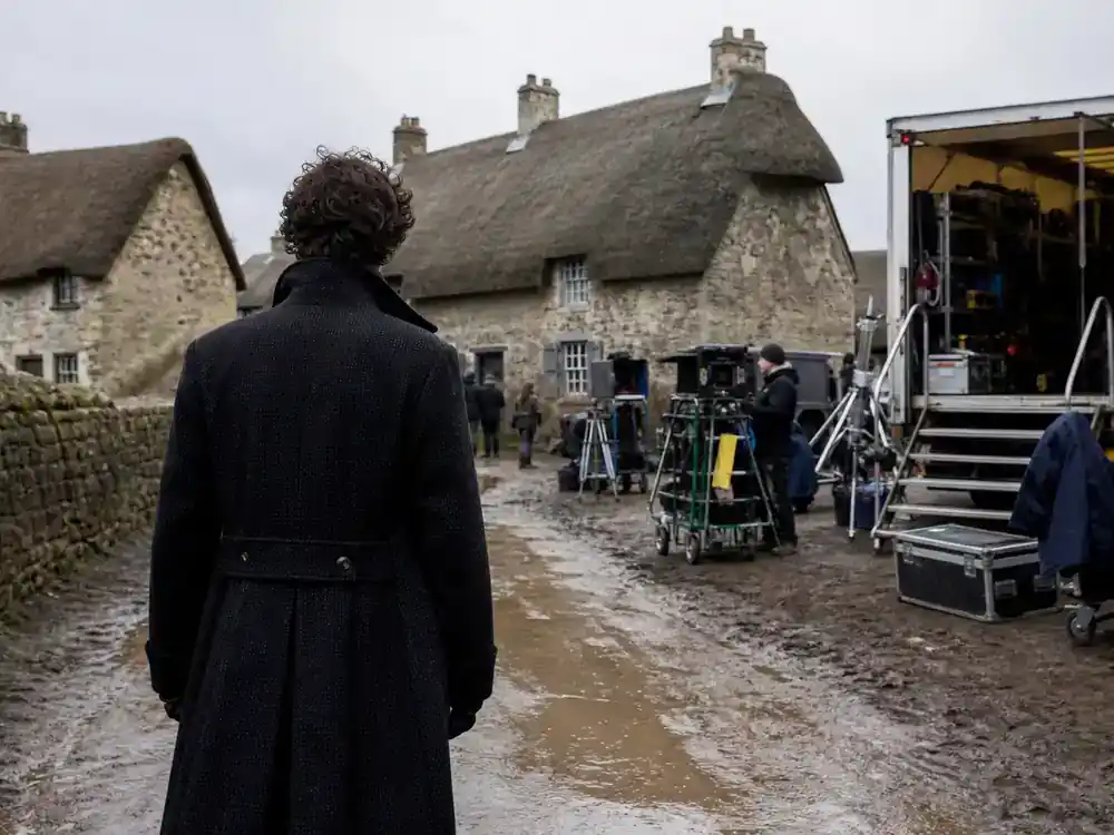 Harry Potter cast net worth 2026 ranked Rupert Grint — actor silhouette from behind on rustic cottage film location with production trucks