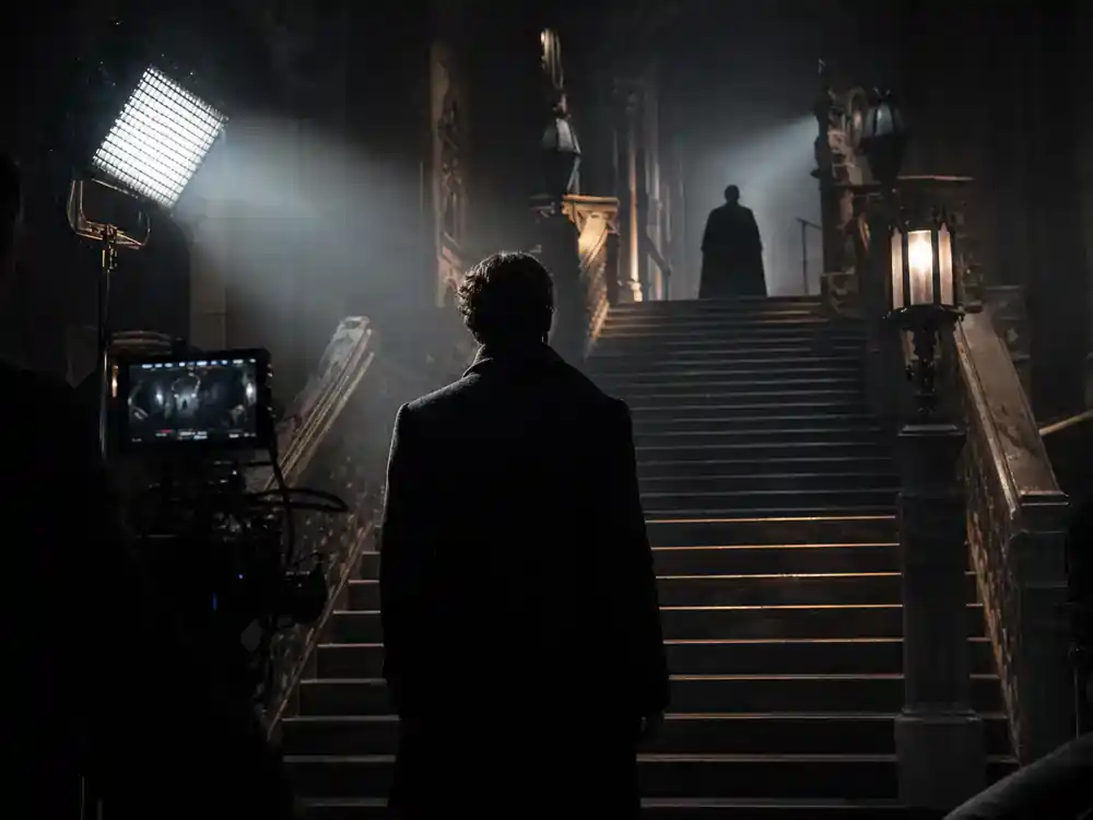 Harry Potter Fantastic Beasts cast guide Grindelwald — dark antagonist silhouette from behind on gothic stone staircase film set with production lights