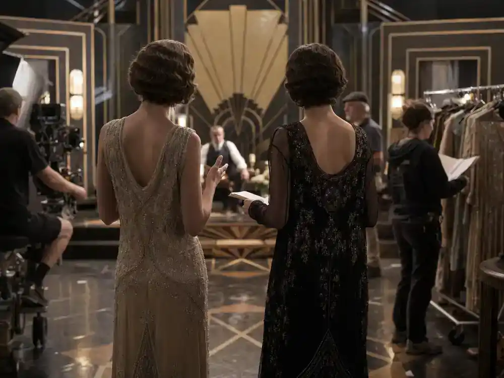 Harry Potter Fantastic Beasts cast guide Goldstein sisters — two actress silhouettes from behind in 1920s dresses rehearsing on Art Deco film set