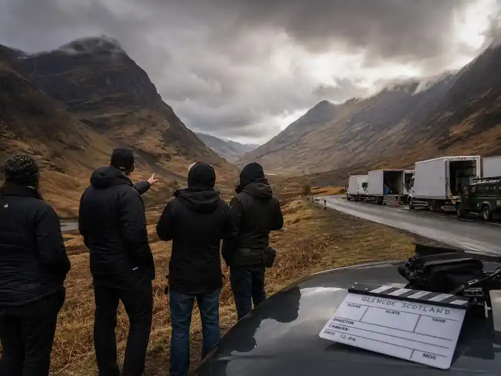 Harry Potter filming locations in Scotland guide Glencoe — director and crew silhouettes scouting dramatic mountain valley film location with production trucks
