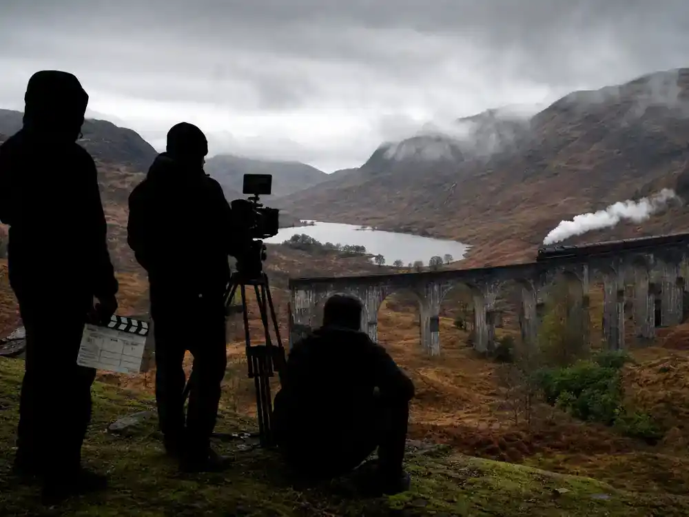 Harry Potter filming locations in Scotland guide Glenfinnan Viaduct — steam train on Highland bridge with film crew scouting misty glen location