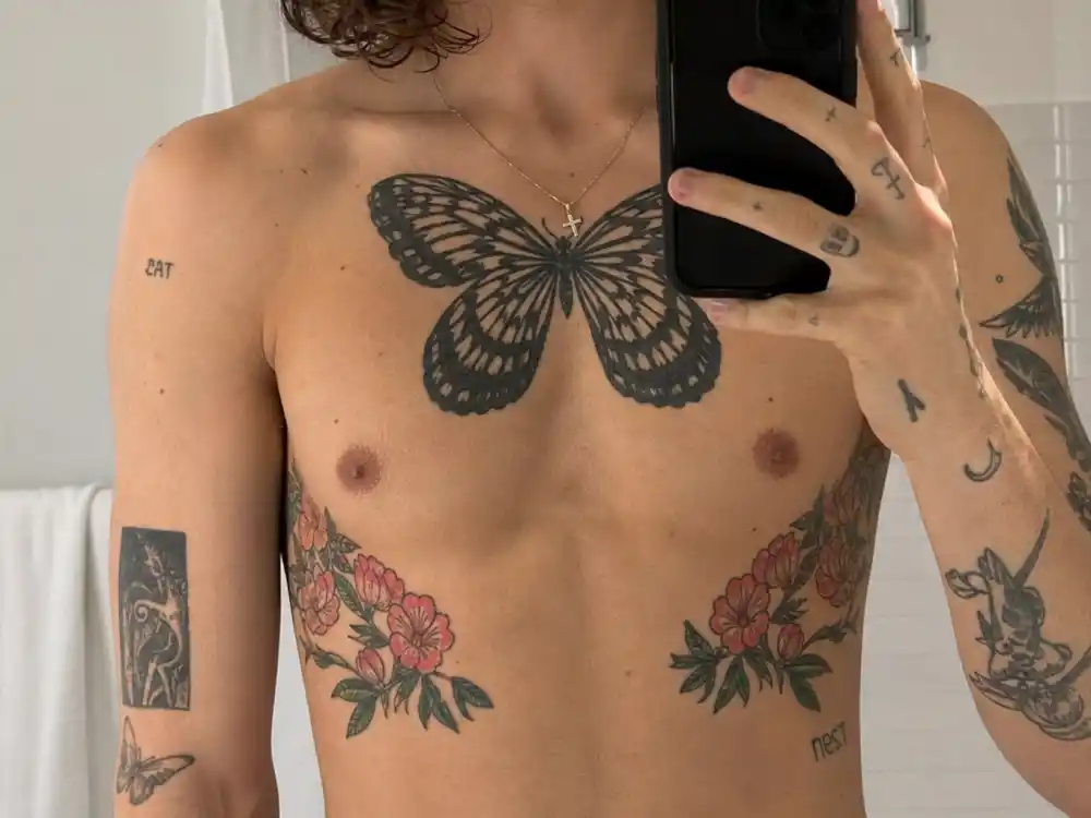 Harry Styles tattoos and their meanings butterfly chest — large black butterfly tattoo on tattooed chest and rib floral ink mirror close-up