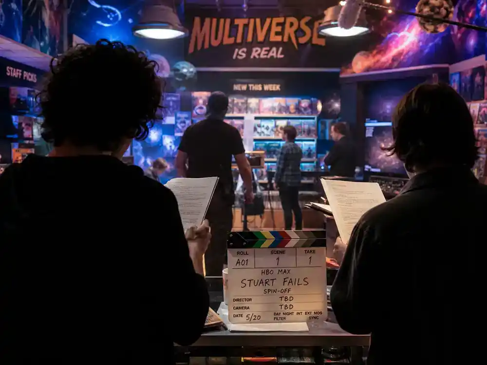 HBO Max new series July 2026 guide Stuart Fails to Save the Universe — actor silhouettes from behind on comic book store TV comedy soundstage with clapperboard