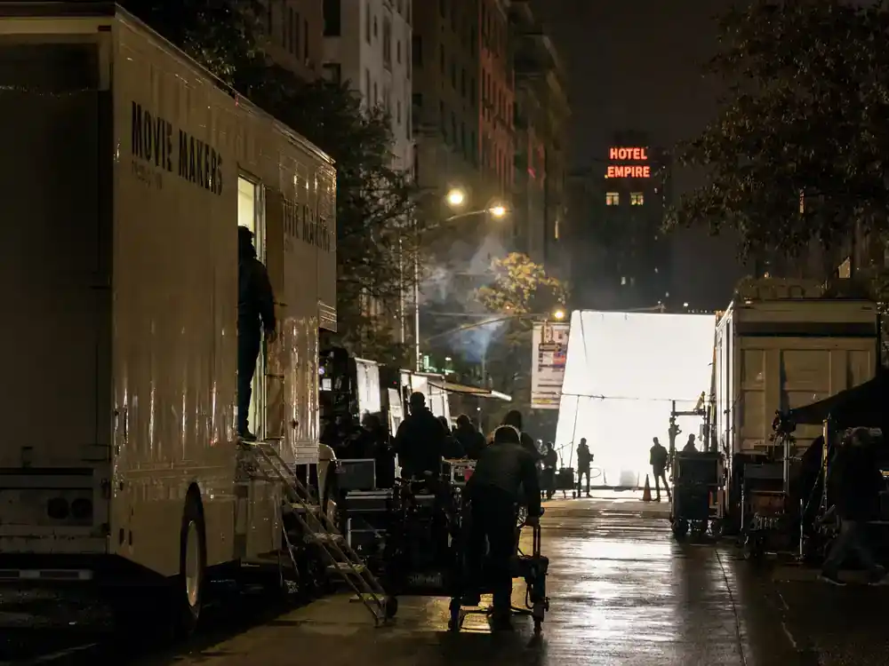 highest paid actors in Hollywood 2026 ranked blockbuster pay — night location filming with film trucks and crew silhouettes unloading equipment