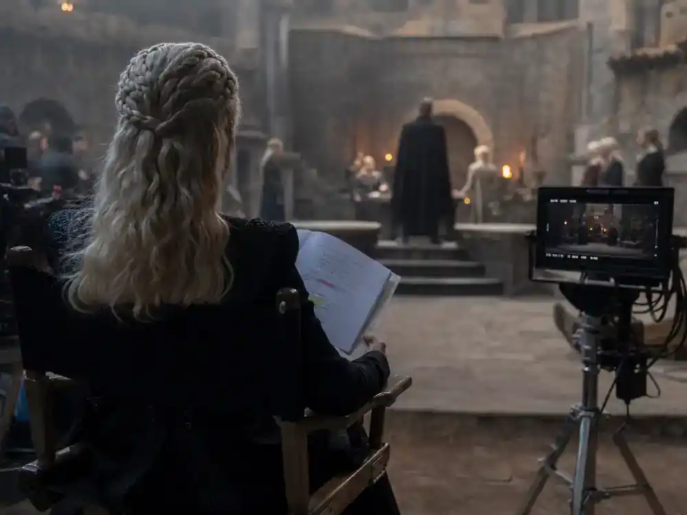 House of the Dragon season 3 cast guide Rhaenyra — actress silhouette from behind on director chair reviewing script on castle film set