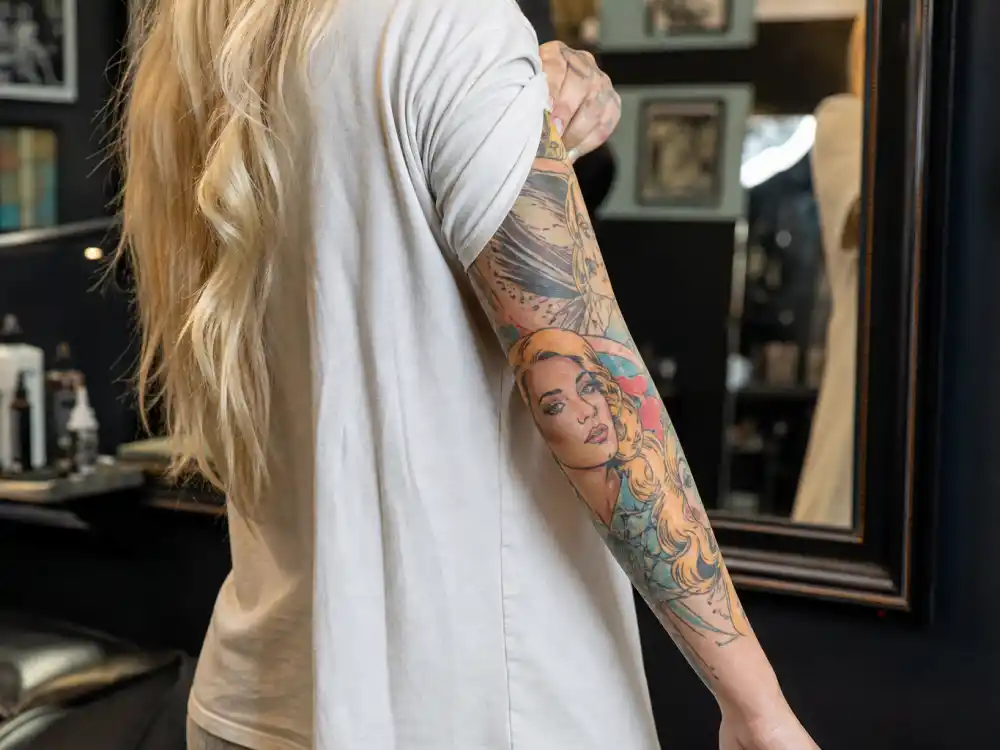 Iggy Azalea tattoos and their meanings Birth of Venus — colorful cartoonish goddess portrait forearm tattoo covering old flower design