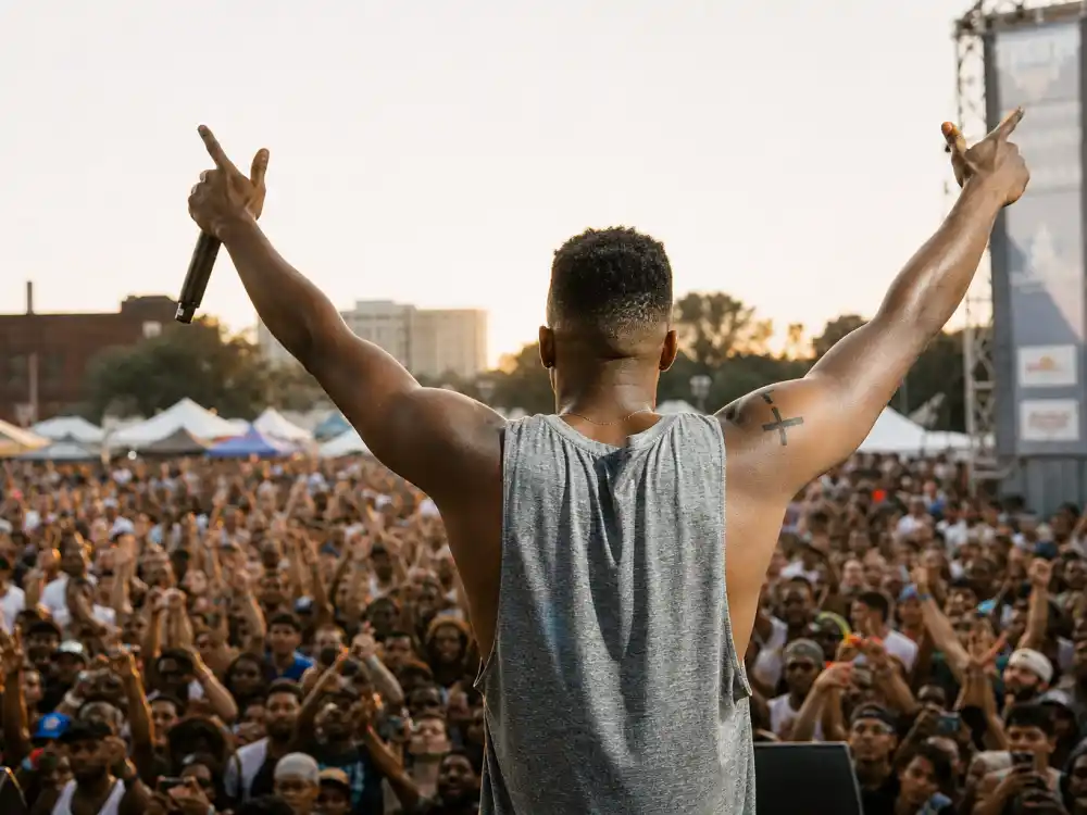 J Cole tattoos and their meanings — festival performance from behind with cross tattoo visible on left arm under golden hour stage lights
