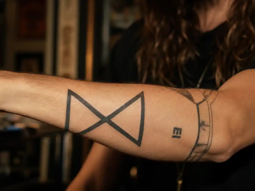 Jared Leto tattoos and their meanings — Echelon X geometric symbol on left forearm close-up in tattoo studio