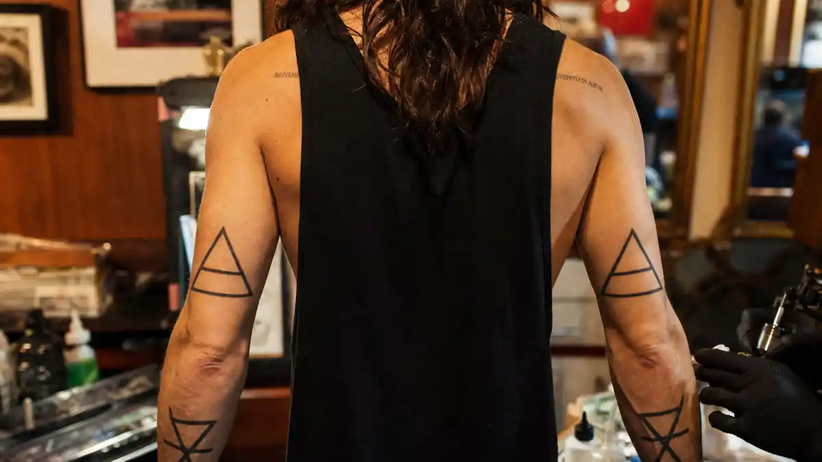 Jared Leto tattoos and their meanings — rock frontman seen from behind in tattoo studio with geometric forearm and back ink visible