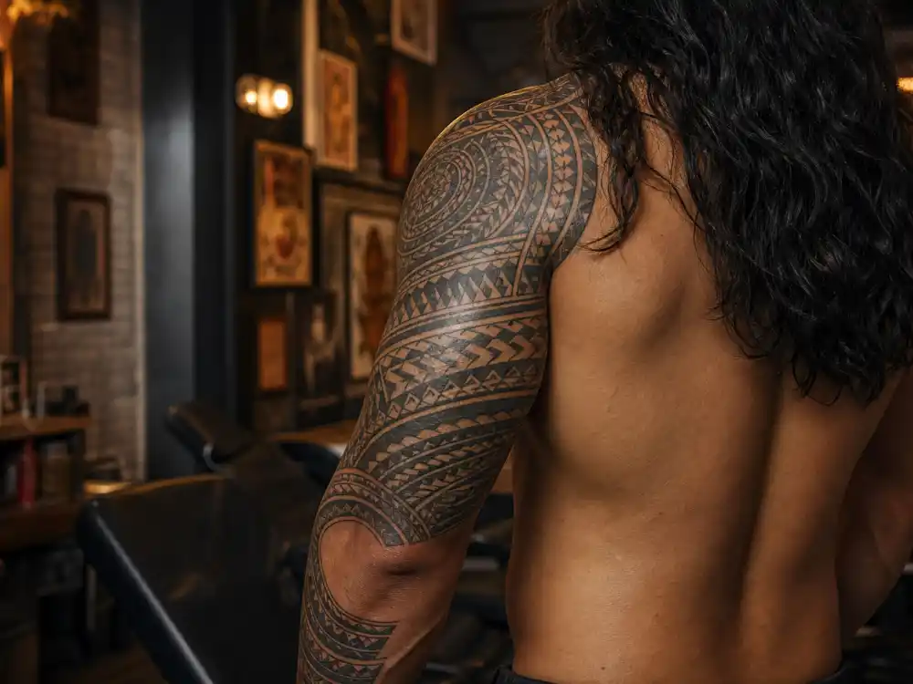 Jason Momoa tattoos and their meanings arm sleeve — full Polynesian tribal sleeve from elbow to shoulder in tattoo studio back view