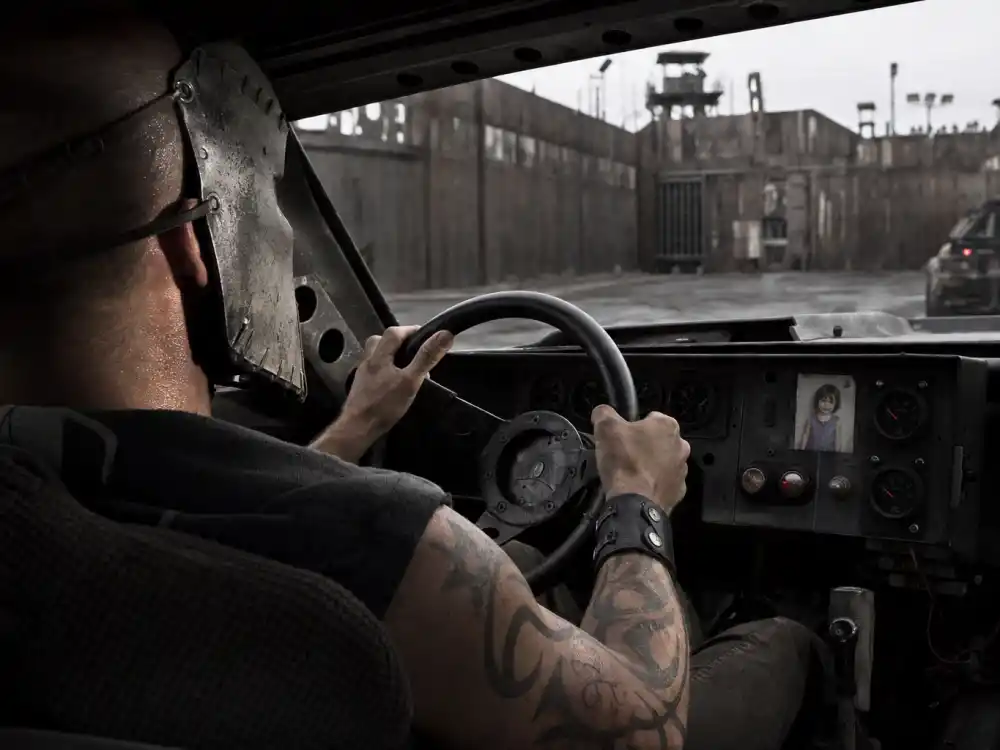 Jason Statham tattoos and their meanings — Frankenstein steel racing mask with tribal character tattoos on forearms in race car