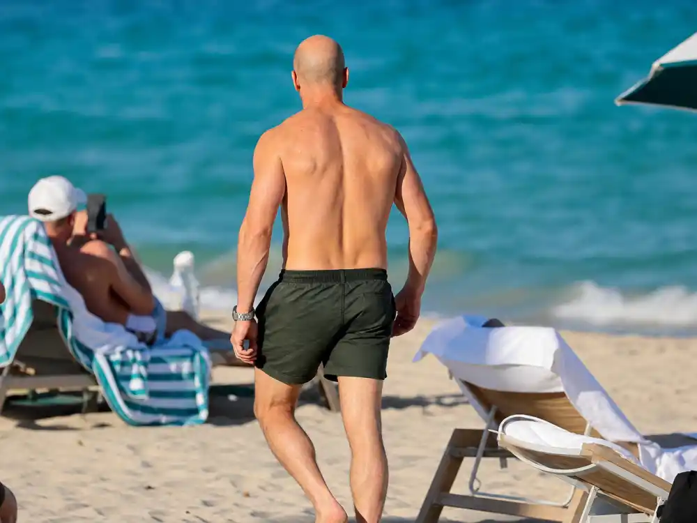 Jason Statham tattoos and their meanings — shirtless action star from behind on Miami beach with clean untattooed back and shoulders