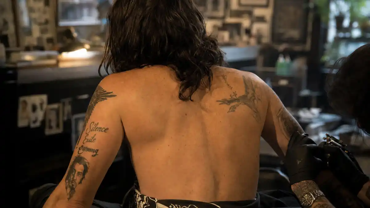 Johnny Depp tattoos and their meanings — bohemian actor seen from behind in tattoo studio with script and portrait ink visible on both arms