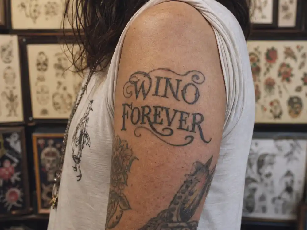 Johnny Depp tattoos and their meanings — close-up of altered WINO FOREVER script tattoo on right upper arm after Winona Forever modification