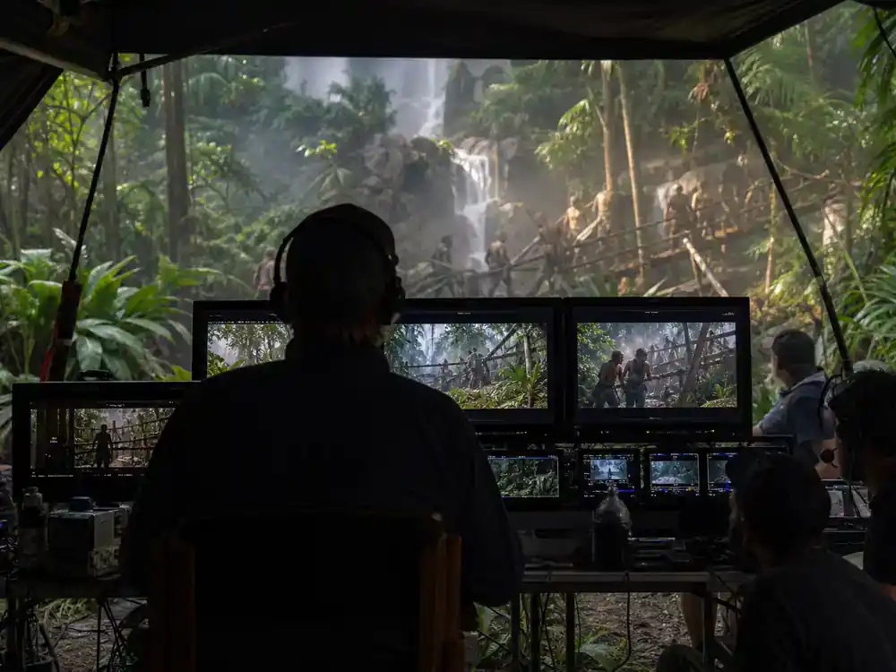 Jurassic World Rebirth cast and characters guide Gareth Edwards — director reviewing monitors at jungle location video village tent from behind