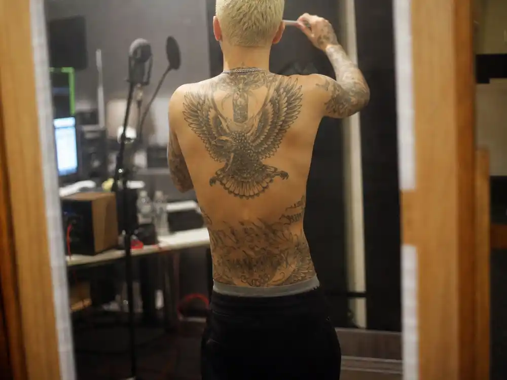 Justin Bieber tattoo collection guide stomach eagle — large eagle tattoo and Son of God script across abdomen on young slim male with bleached blonde hair mirror selfie angle