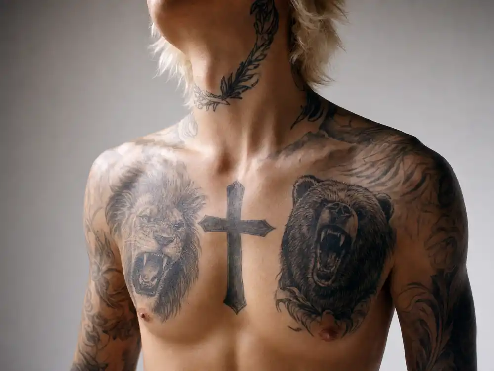Justin Bieber tattoos and their meanings chest cross — ornate gothic cross and Son of God script tattoo on slim male torso with bleached blonde hair