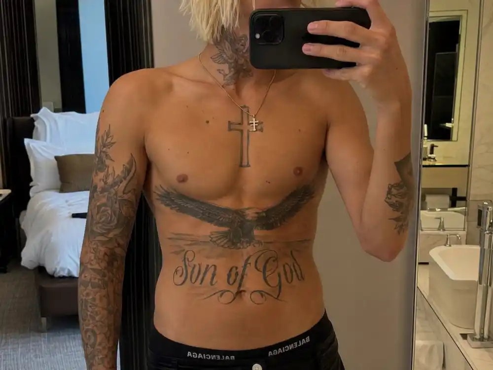 Justin Bieber tattoos and their meanings stomach eagle — large eagle tattoo and Son of God script across abdomen on young slim male with bleached blonde hair mirror selfie angle