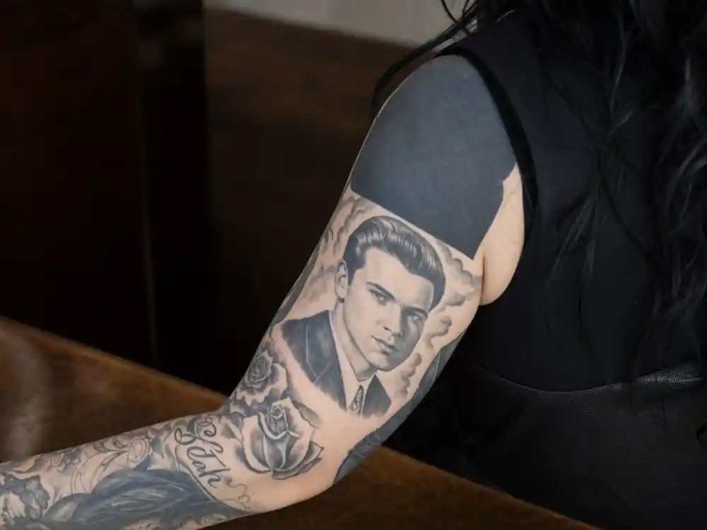 Kat Von D tattoos and their meanings — black-and-grey father portrait tattoo on forearm surrounded by solid blackout ink panels