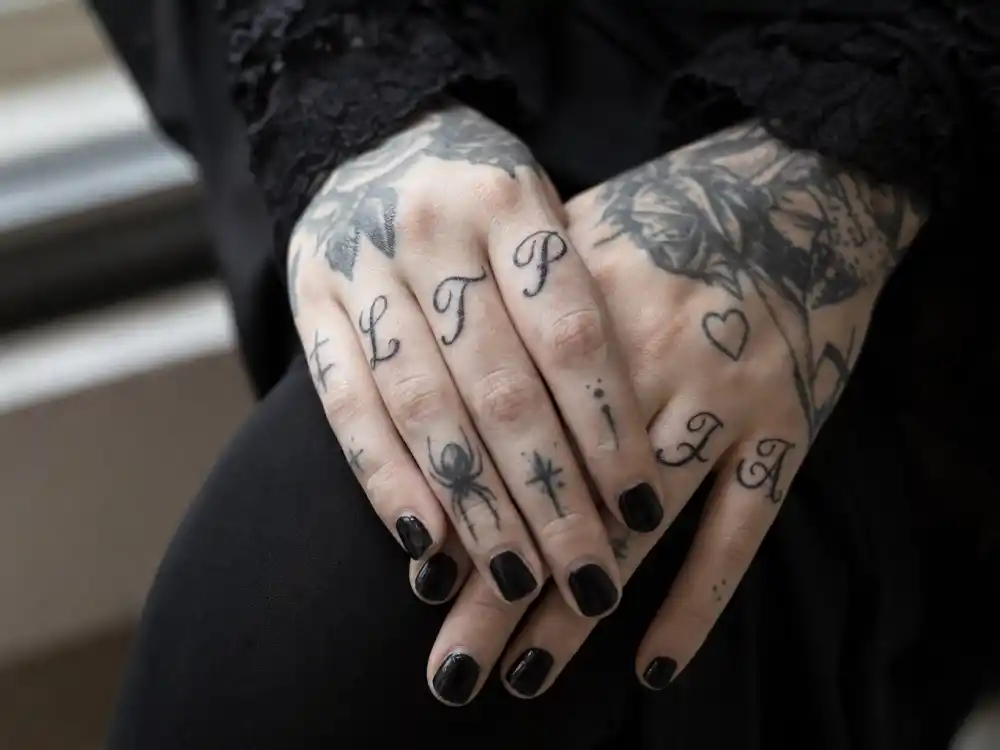 Kat Von D tattoos and their meanings — close-up of LTP and TLA finger script tattoos with spider and heart symbols on inked hands